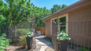 Un espace patio agrémenté d’un chemin en pierre, d’une porte en métal et de plantes en pot.