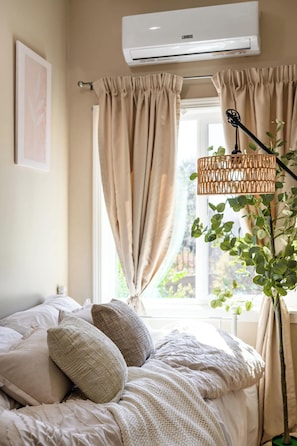 A bedroom with a bed, beige curtains, a window, and an air conditioning unit. - Modern Cozy Stay w Outdoor Patio & Grill (Pomona)