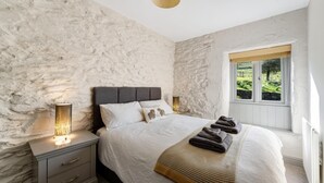 Ein Schlafzimmer mit Steingemäuer, einem Bett mit weißer Bettwäsche, zwei Nachttischlampen, einem Fenster mit Aussicht und einer Heizung.