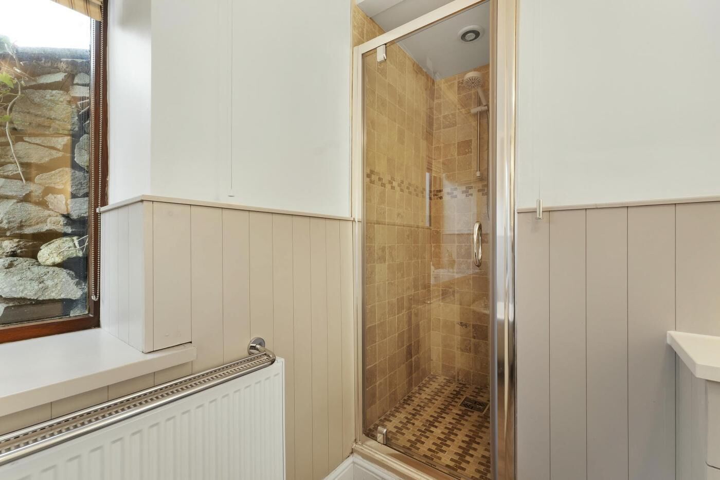 A shower with a glass door, a stone wall outside, and a white radiator.