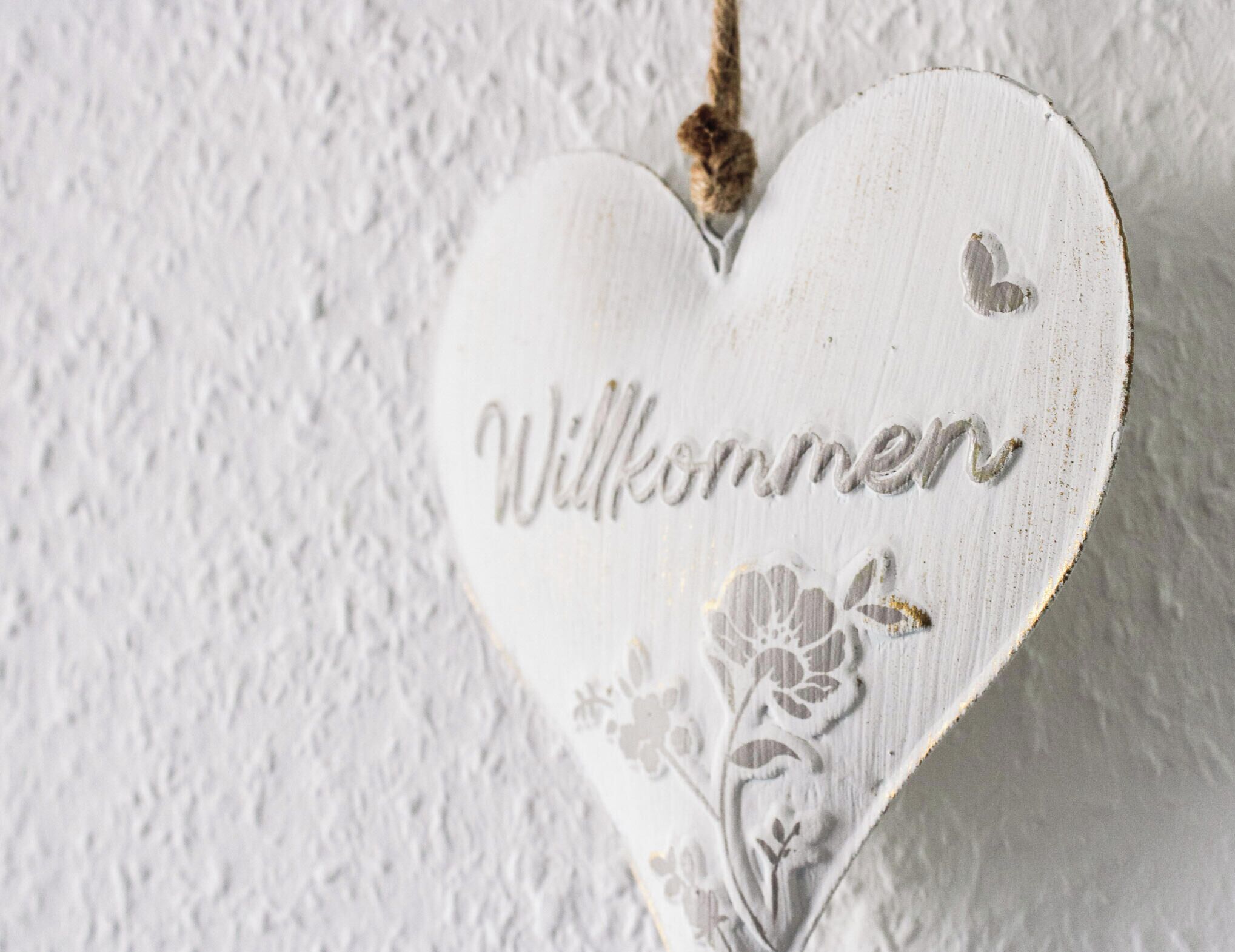 A white heart-shaped decoration with the word 'Willkommen' and floral designs.