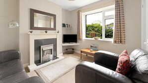 A living room with a fireplace, a television, and a window with curtains. - 2 Bed in Ambleside (oc-lr141) (Ambleside)