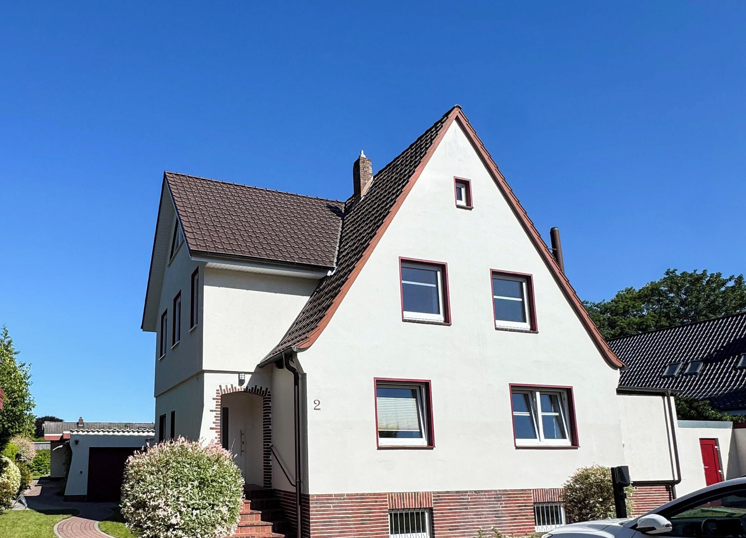 Ein zweistöckiges Haus mit steiler Satteldach und Ziegelkeller, sowie einer Garage.