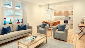 Una sala de estar moderna con un sofá, sillones, una mesa de centro y un comedor con una mesa y sillas.