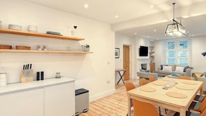Una cocina moderna con estantes de madera, una zona de comedor con mesa y sillas, y una sala de estar con sofá y televisor.