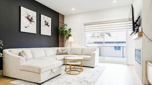 A modern living room with a sectional sofa, a small round table, a potted plant, and artwork on the wall. - Stampede Last Minute Deal 3BR Home Downtown Patio & AC (Calgary)