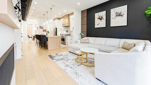 A modern living room with a sofa, a coffee table, and a kitchen in the background. - Stampede Last Minute Deal 3BR Home Downtown Patio & AC (Calgary)