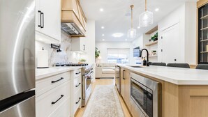 A modern kitchen with white cabinetry, stainless steel appliances, and pendant lighting. - Stampede Last Minute Deal 3BR Home Downtown Patio & AC (Calgary)