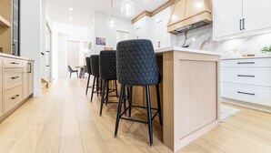 A modern kitchen with wooden cabinets, a marble countertop, and black bar stools. - Stampede Last Minute Deal 3BR Home Downtown Patio & AC (Calgary)