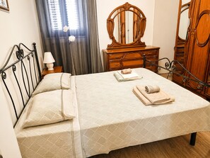 A neatly made bed with a patterned bedspread, a wooden dresser with a mirror, and a nightstand with a lamp. - Domus Clesia (Ostuni)