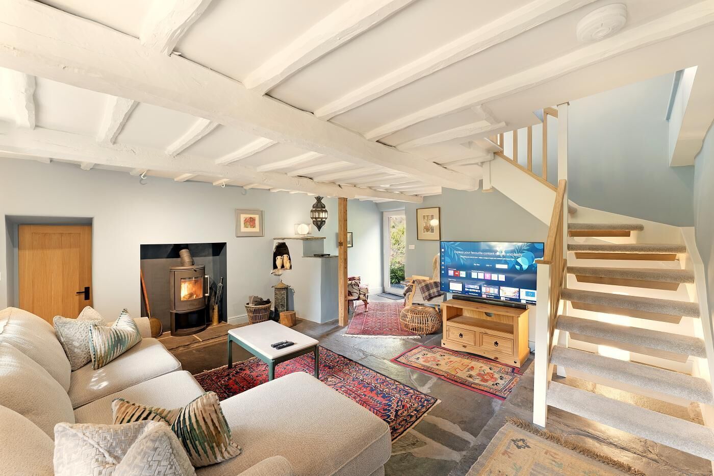 A cozy living room with a fireplace, a television, and a staircase.