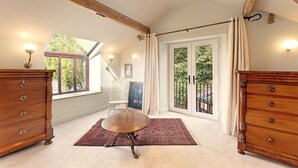 Une pièce comprenant une commode en bois, une chaise, une table ronde, un tapis, une fenêtre et une porte avec des panneaux de verre.