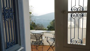 A balcony with a table and chairs, a view of the mountains, and a door with decorative metalwork.