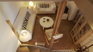 A room with a sofa, a round table, a chair, a lamp, and a bookshelf.