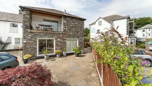 Une maison en pierre à deux étages, dotée d’un balcon, de plantes en pot et d’une clôture en bois.