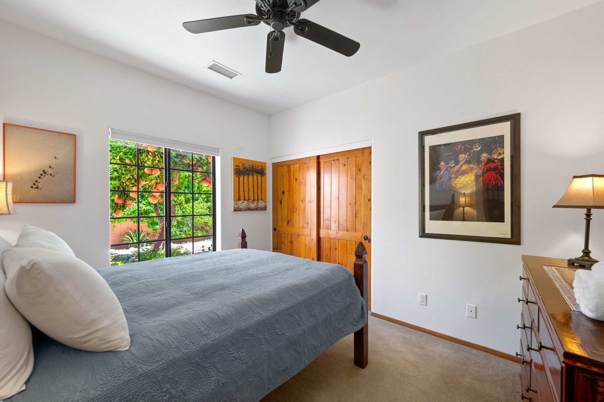 Une chambre à coucher avec un lit, un ventilateur de plafond, une fenêtre donnant sur des arbres et une porte.