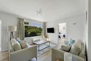 Un salon moderne comprenant un canapé, des fauteuils, une table basse, un téléviseur et une grande fenêtre avec des rideaux.