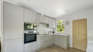 Een moderne keuken met witte kastjes, een ingebouwde oven, een spoelbak en een raam met uitzicht op groen.