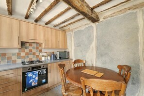 A kitchen with wooden cabinets, a microwave, a stove, and a dining table with chairs. - 2 Bed in Hawkshead (oc-lr062) (Hawkshead)