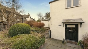 Ein Cottage mit Steinaußenwand, einer schwarzen Tür und einem Schild mit der Aufschrift 'FLAG COTTAGE'.