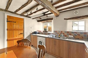 Una cocina con armarios de madera, lavadora, pileta y ventana con vista.