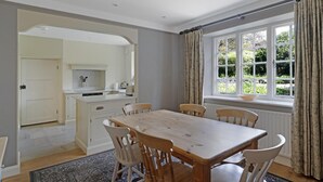 A dining area with a wooden table and chairs, a kitchen with white cabinets, and a window with curtains. - 3 Bed in Ambleside (oc-lr042) (Ambleside)