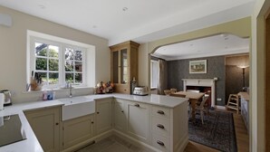 A kitchen with a large island, a dining area with a fireplace, and a view of the outdoors through a window. - 3 Bed in Ambleside (oc-lr042) (Ambleside)