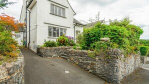 A white two-story house with a stone wall and a paved driveway. - 3 Bed in Ambleside (oc-lr042) (Ambleside)