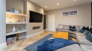 Een moderne woonkamer met een flatscreen televisie, een grijze bank, een houten salontafel en een visgraatvloer.