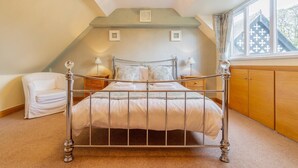 A bedroom with a metal bed frame, a white sofa, wooden cabinets, and a window with a view of a house. - 3 Bed in Ambleside (oc-lr214) (Claife)