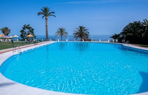 Ein klares, blaues Schwimmbecken mit Blick aufs Meer, umgeben von Palmen und Sonnenschirmen.