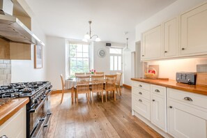 A kitchen with a gas stove, wooden chairs, a dining table, and white cabinets. - 4 Bed in Ambleside (oc-lr055) (Ambleside)