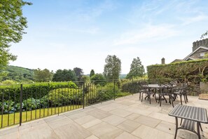 A patio with a table and chairs, surrounded by a metal fence and a view of a green landscape. - 4 Bed in Ambleside (oc-lr055) (Ambleside)