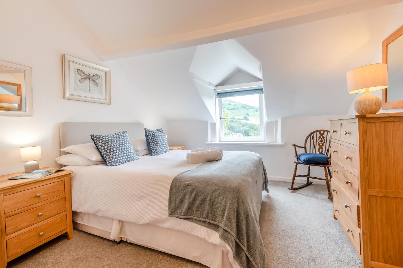 Une chambre à coucher comprenant un lit, une table de chevet, une commode, une chaise et une fenêtre donnant sur un beau paysage.