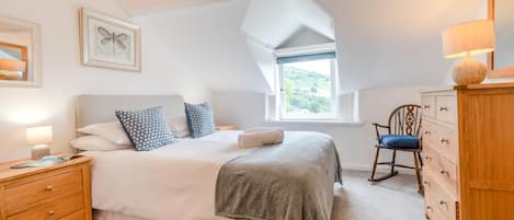 A bedroom with a bed, a nightstand, a dresser, a chair, and a window with a view.