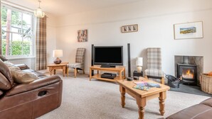 Una sala de estar con un sofá de cuero, televisor, chimenea y una ventana con cortinas.