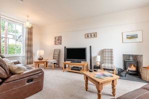 A living room with a leather sofa, a television, a fireplace, and a window with curtains. - 4 Bed in Ambleside (oc-lr055) (Ambleside)