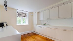 Eine Küche mit weißen Schränken, einem Fenster mit Blumenmuster und Holzboden.