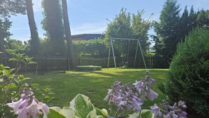 A garden with a swing set, a wooden fence, and various plants. - Bungalow Boddenhaus with Private Terrace, Garden, and Wi-Fi (Sundhagen)