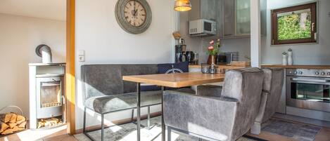 A modern kitchen with a dining area, including a wooden table, grey upholstered chairs, and pendant lighting.