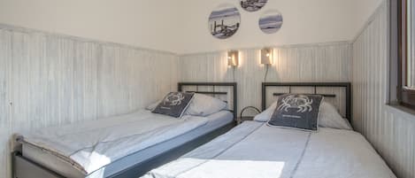 A bedroom with two single beds, each with a pillow featuring a crab design, and a wall-mounted light fixture above the beds.