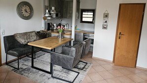 A compact living space with a dining area, kitchenette, and a door. - Bungalow Boddenhaus with Private Terrace, Garden, and Wi-Fi (Sundhagen)