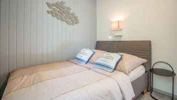 Un dormitorio con una cama, almohadas, una lámpara de pared y una mesita.