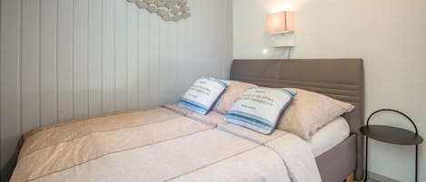 A bedroom with a bed, pillows, a wall-mounted lamp, and a small table.