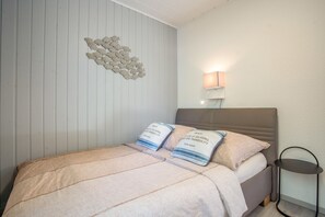 Une chambre à coucher avec un lit, des oreillers, une lampe fixée au mur et une petite table.