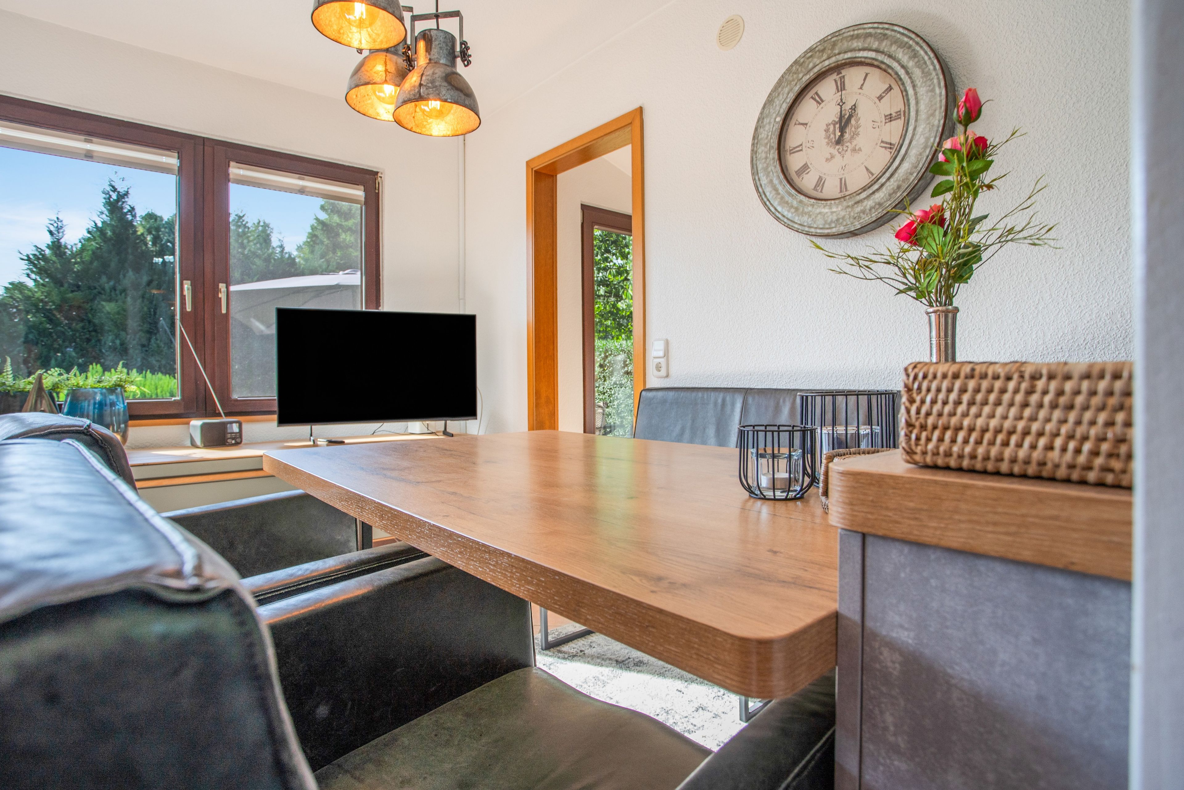 Una sala de estar moderna con una mesa de comedor de madera, un televisor de pantalla plana, un sofá y un reloj de pared.