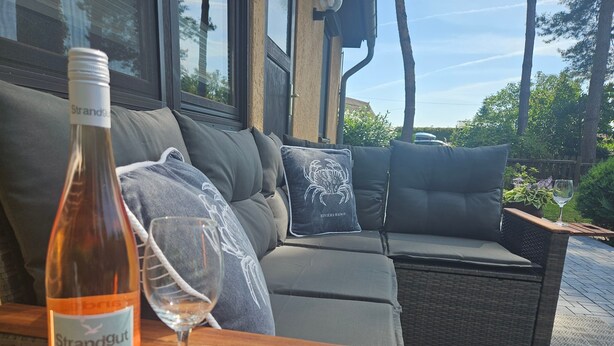 A wicker outdoor seating area with a bottle of wine and a glass on a table. - Bungalow Boddenhaus with Private Terrace, Garden, and Wi-Fi (Sundhagen)