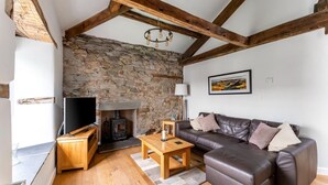 A cozy living room with a stone wall, wooden beams, a fireplace, a leather sofa, and a television. - 1 Bed in Ambleside (oc-lr160) (Ambleside)