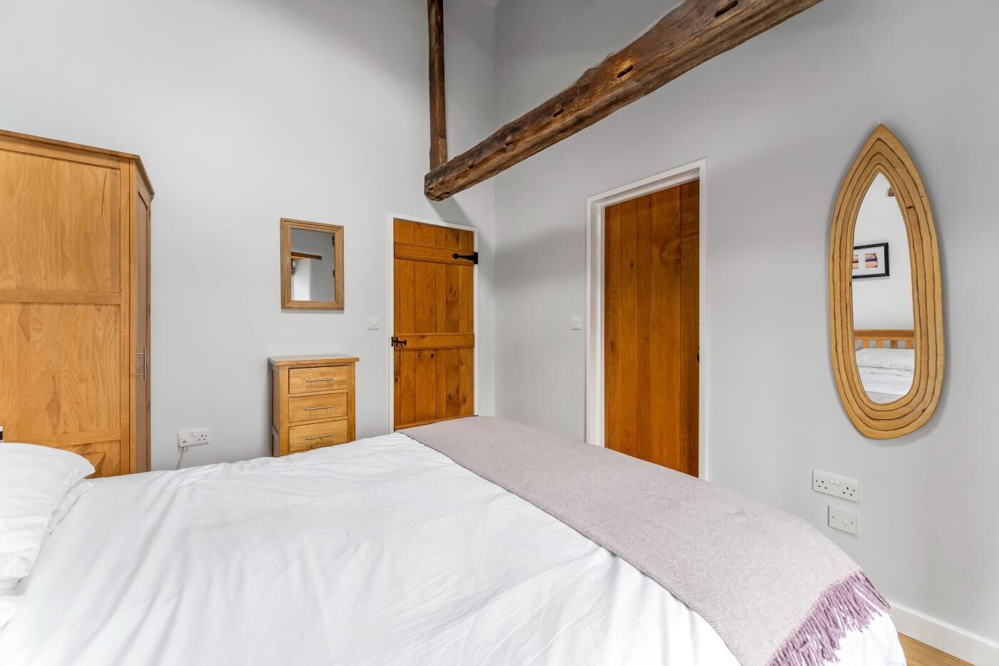 Une chambre à coucher avec un grand lit, une armoire en bois, une commode, un miroir et une porte.