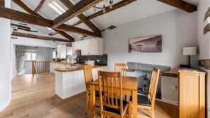 A spacious kitchen with wooden beams, a dining area with a table and chairs, and a fireplace. - 1 Bed in Ambleside (oc-lr160) (Ambleside)